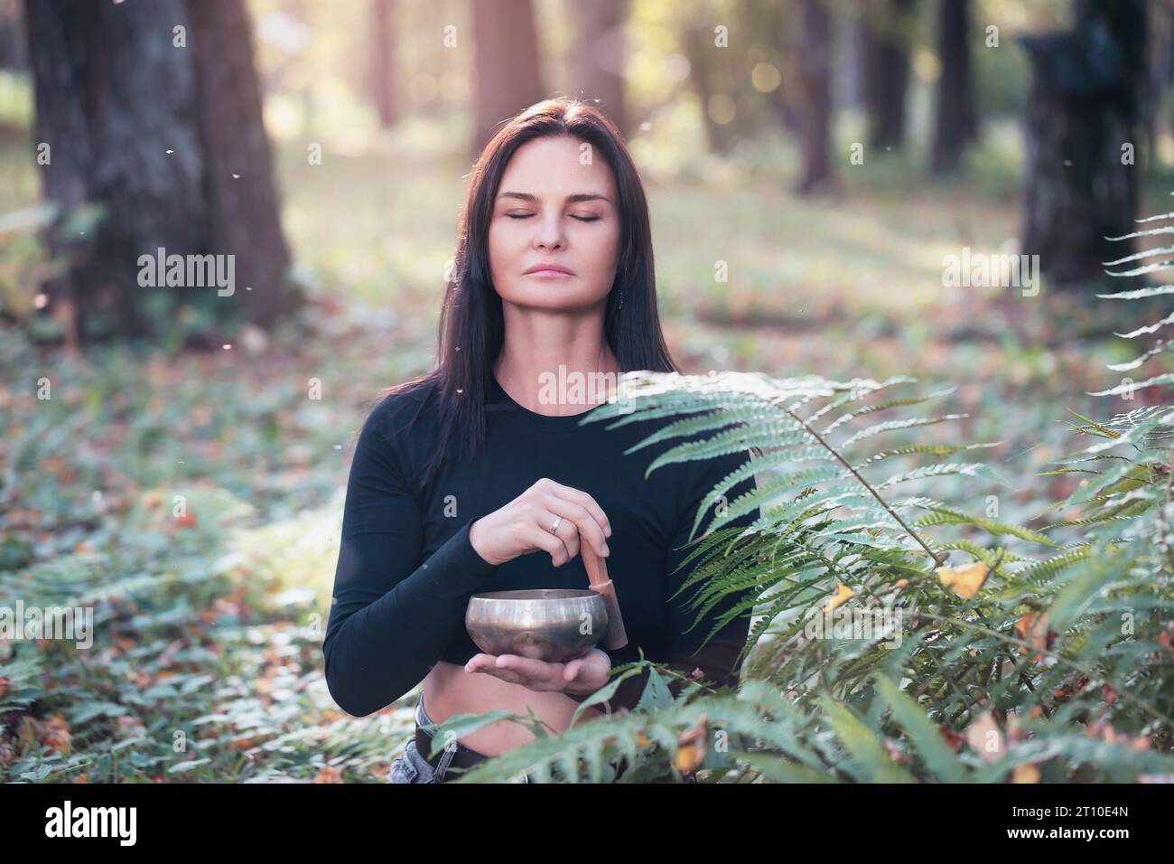 Donna che pratica yoga, fa meditazione sana con una ciotola tibetana, allevia lo stress e migliora le condizioni generali del corpo, si allena con gli occhi Foto Stock