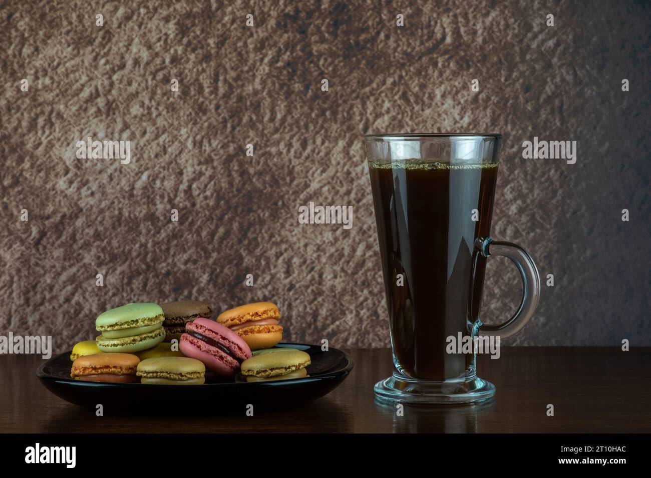 Pila di biscotti macaron e bicchiere di caffè nero su una superficie di legno Foto Stock