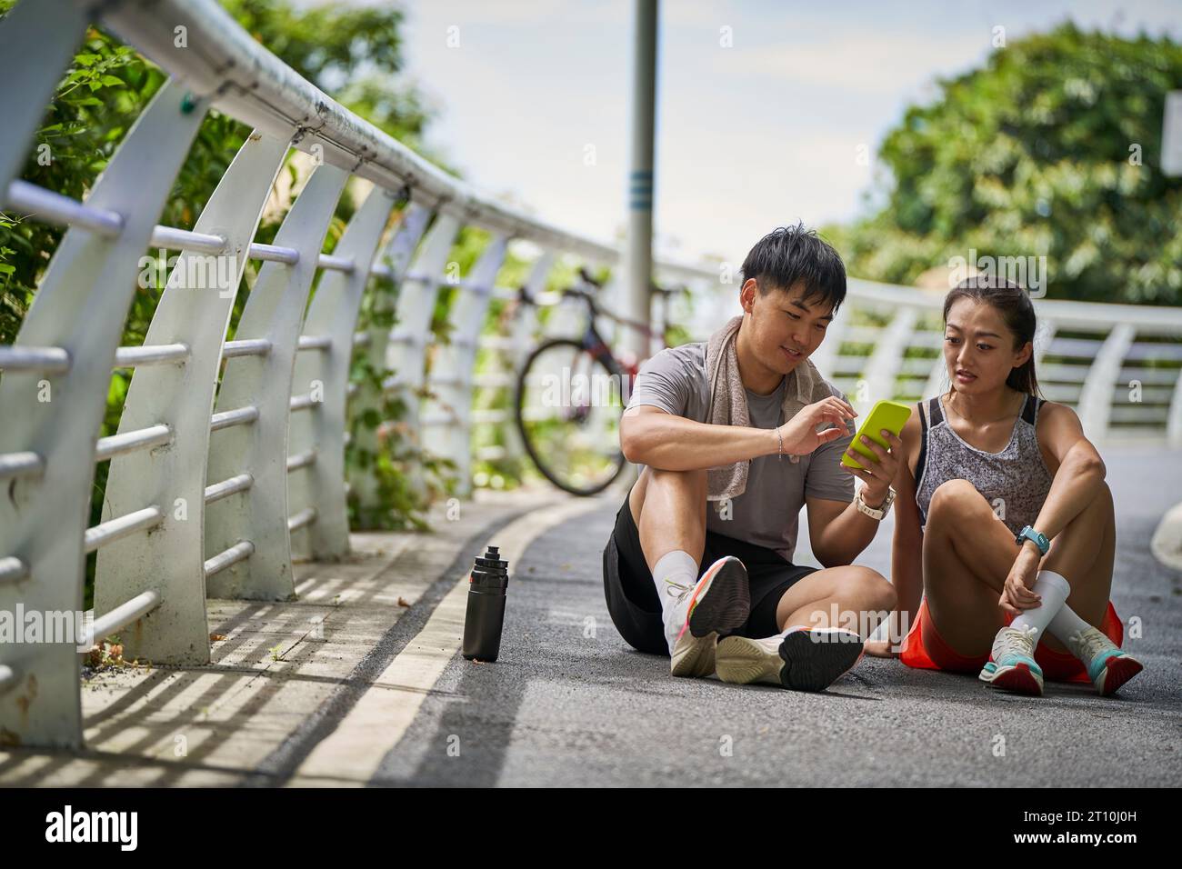 giovani coppie asiatiche che condividono le foto del cellulare mentre fanno una pausa durante gli esercizi all'aperto Foto Stock