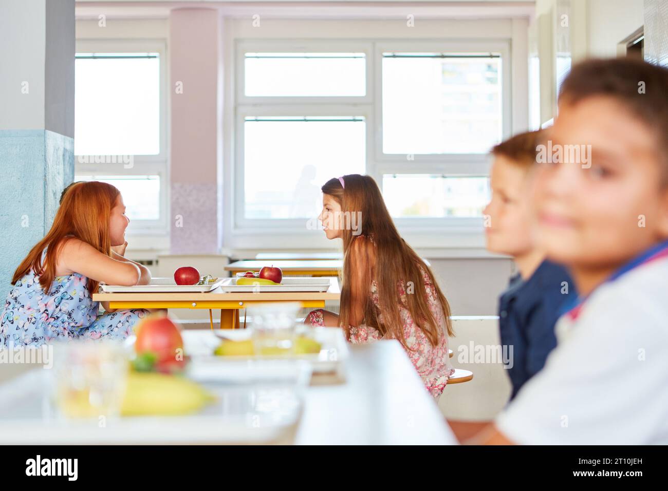 Vista laterale degli studenti seduti e chiacchierando con vassoi di cibo sul tavolo della caffetteria a scuola Foto Stock