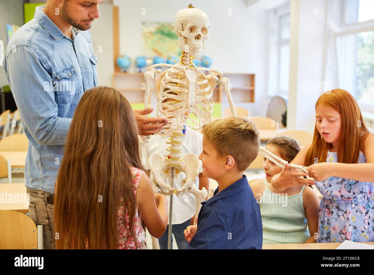 Insegnante maschile e studenti in piedi intorno allo scheletro umano in classe Foto Stock