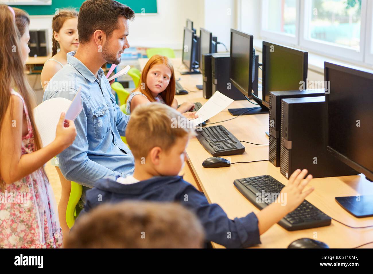 Insegnante di sesso maschile che insegna la codifica ai bambini mentre si è seduti in una classe di computer Foto Stock