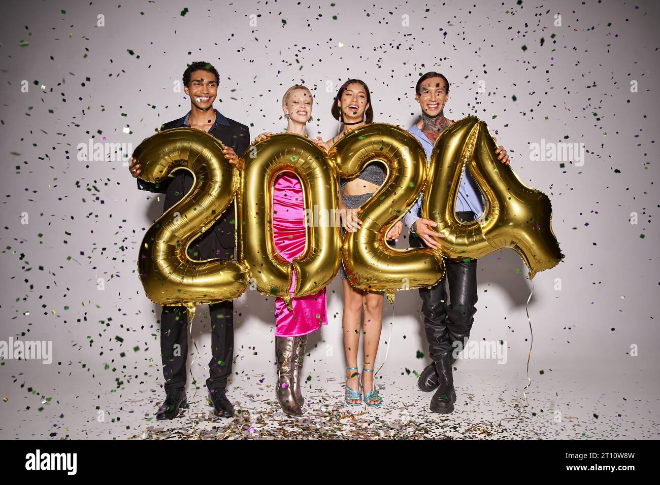 Felici amici interrazziali che tengono palloncini con 2024 numeri vicino alla caduta dei coriandoli, festa di Capodanno Foto Stock