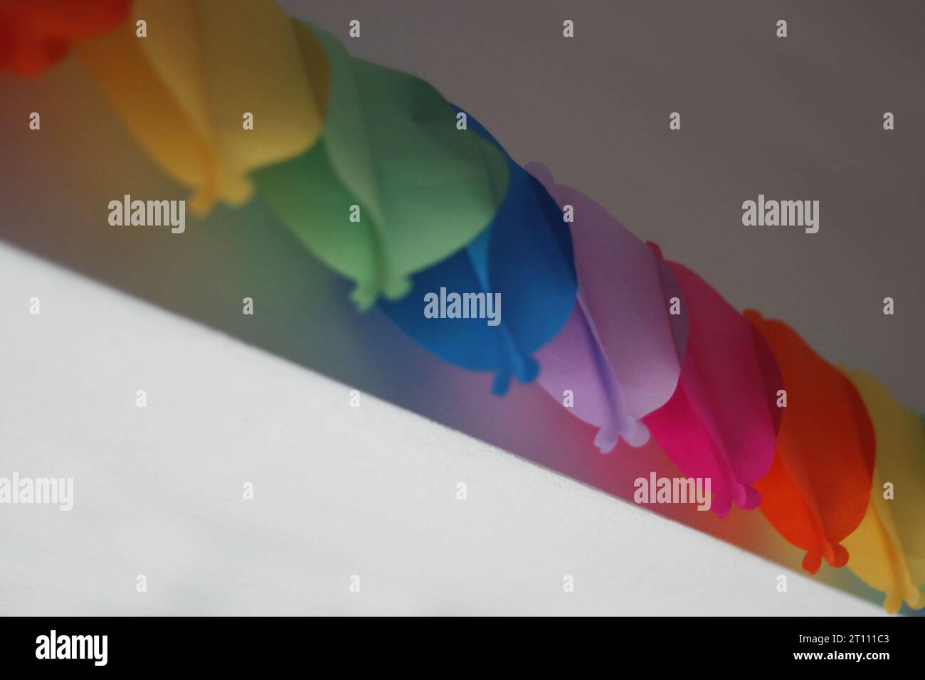 Colorata ghirlanda di compleanno sulla parete bianca sopra la finestra. Facciamo festa. Decorazione murale di compleanno. Catena di carta decorata per le festività sulla parete bianca abov Foto Stock
