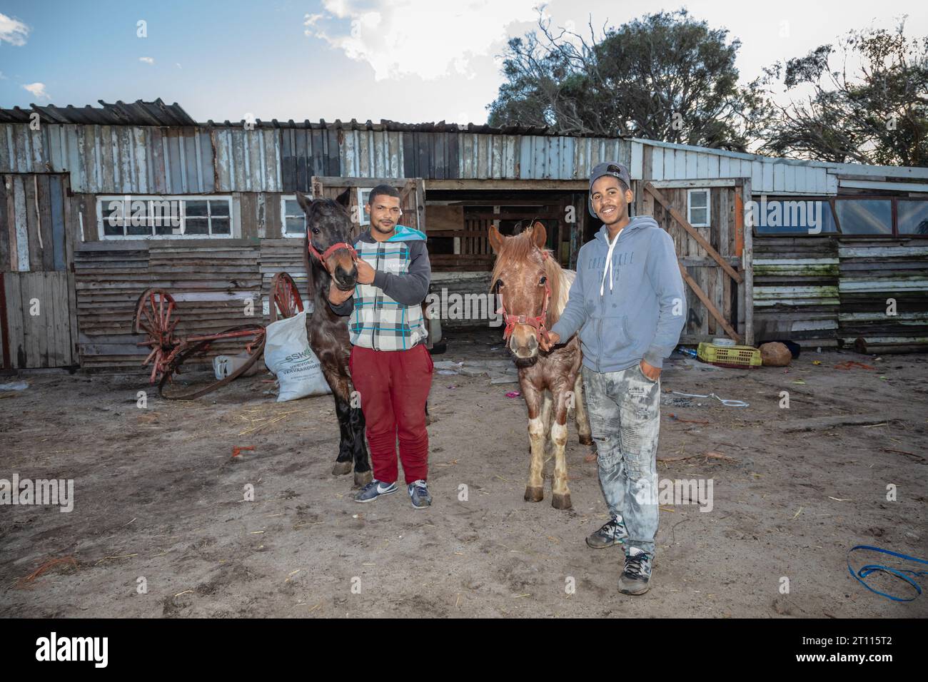 Due giovani uomini di razza mista in piedi accanto ai loro cavalli da carretto, usati per trainare carri per trasportare merci nella comunità povera del Sudafrica Foto Stock