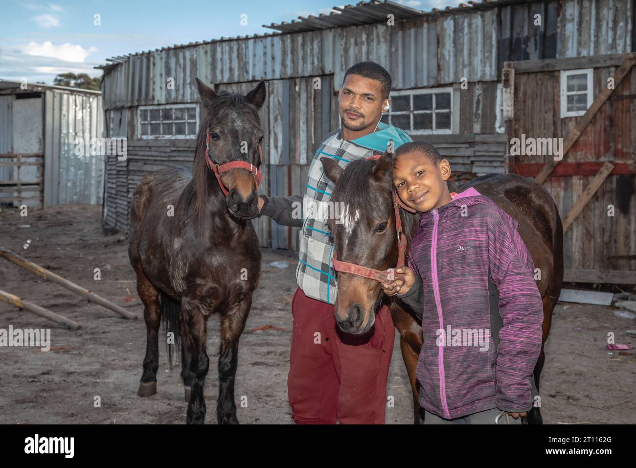 Un uomo e un bambino di razza mista in piedi accanto ai loro cavalli da carro, usati per trainare carrelli per trasportare merci nella comunità povera del Sudafrica Foto Stock