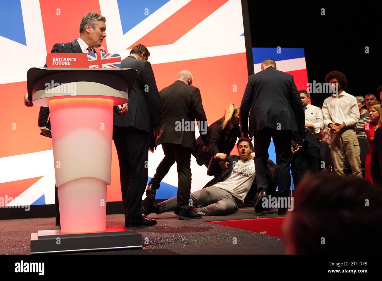 Un manifestante viene trascinato via dopo aver gettato glitter e disturbato il leader laburista Sir Keir Starmer durante il suo discorso di apertura durante la Conferenza del Partito Laburista a Liverpool. Data immagine: Martedì 10 ottobre 2023. Foto Stock