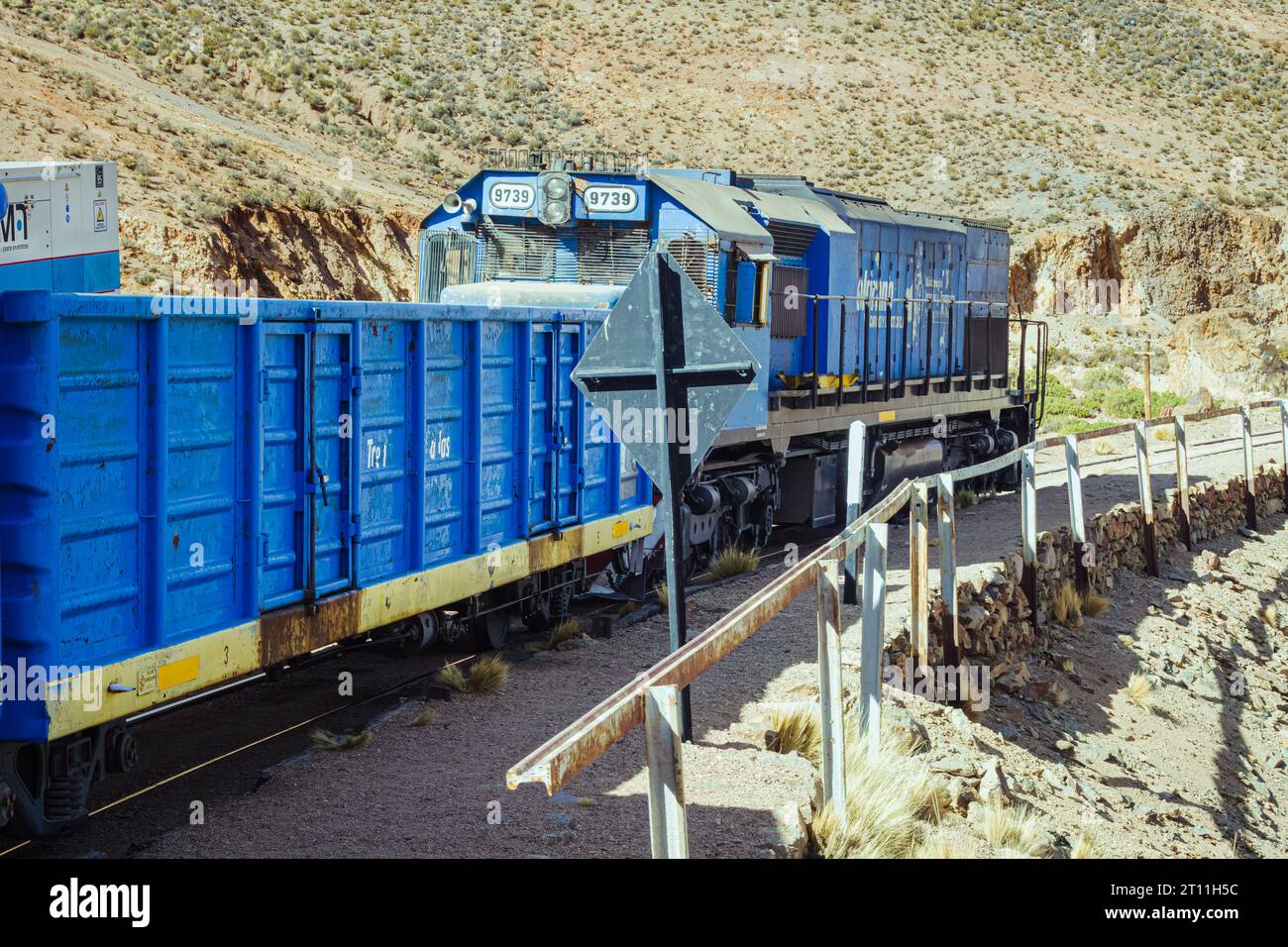 Treno blu elettrico che attraversa la ferrovia, circondato da montagne pittoresche Foto Stock