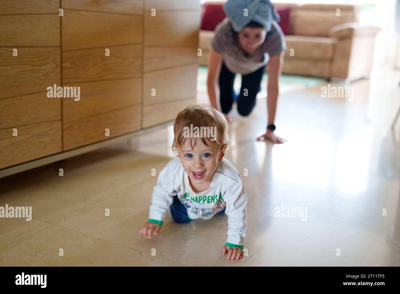 Giocherellando bambino felice che strizza lontano da sua madre durante il tempo di gioco a casa Foto Stock