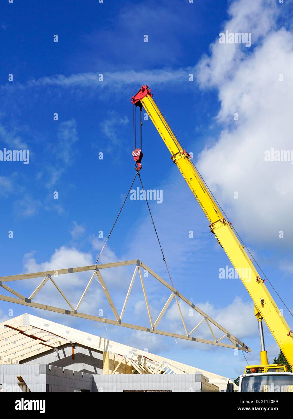 Gru mobile con braccio telescopico giallo che posiziona la capriata in legno del tetto del nuovo edificio, sfondo blu cielo Foto Stock