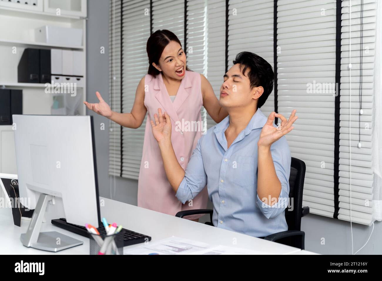 Donna d'affari asiatica arrabbiata urlando e rimproverando un uomo d'affari calmo e meditissimo che fa yoga a mano nell'ambiente dell'ufficio. - Business Fight and Conflict at workplace concept Foto Stock