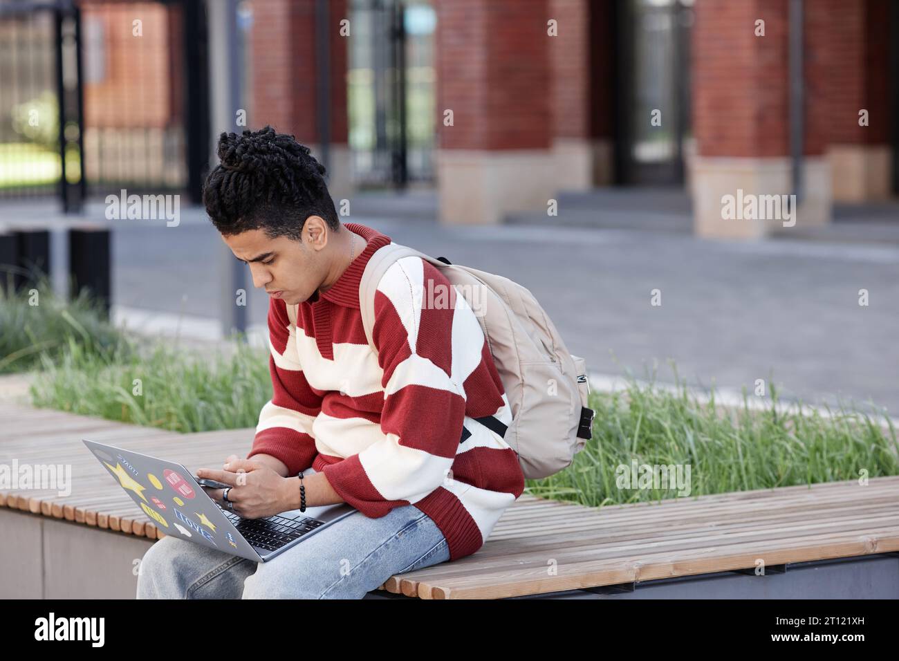 Ritratto laterale di un giovane ragazzo mediorientale che usa un computer portatile all'aperto nel campus universitario, spazio per le copie Foto Stock