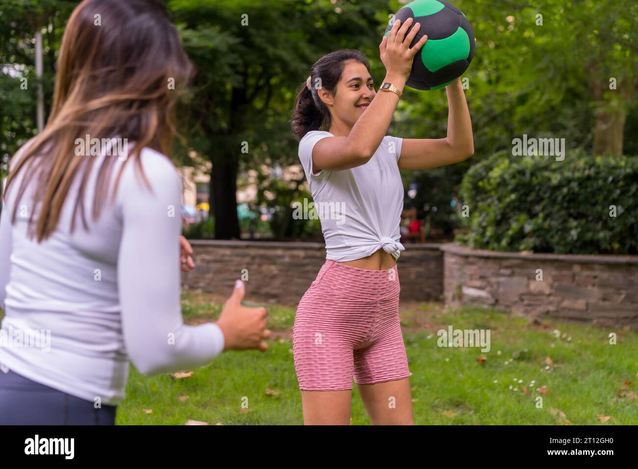 Ragazza latina che fa sport in un parco verde, stile di vita una vita sana, insegnante attento con gli studenti nell'esercizio di squat con la palla di peso Foto Stock