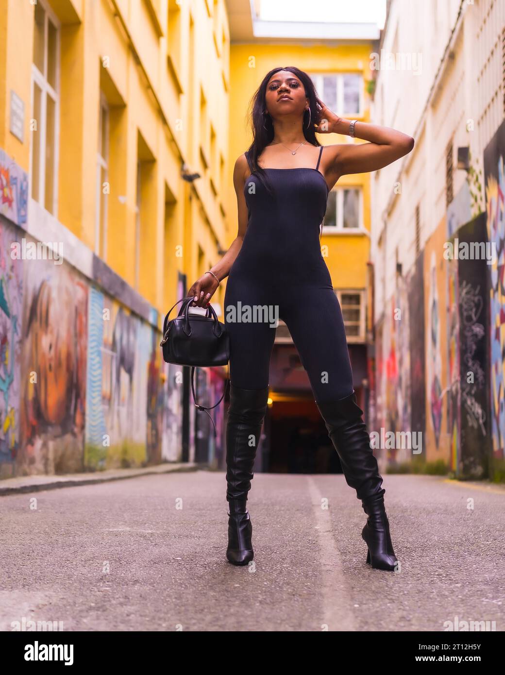 Stile urbano di una ragazza nera alla moda con un completo nero e stivali alti Foto Stock