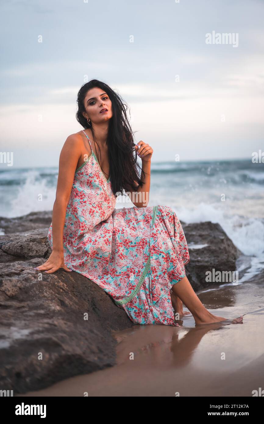 Foto di una bruna caucasica con un vestito di tessuto bianco con fiori, sulla spiaggia in mare godendo le vacanze Foto Stock