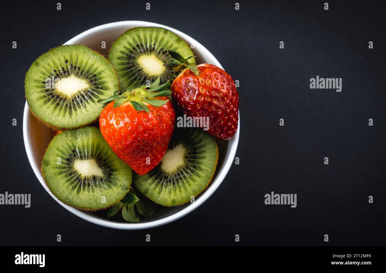 Kiwi e fragole tagliati a fette in un recipiente bianco con sfondo nero Foto Stock