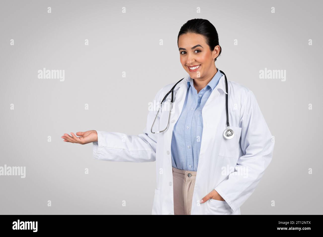 Felice medico latino che presenta un oggetto invisibile sul palmo della mano su sfondo grigio dello studio Foto Stock