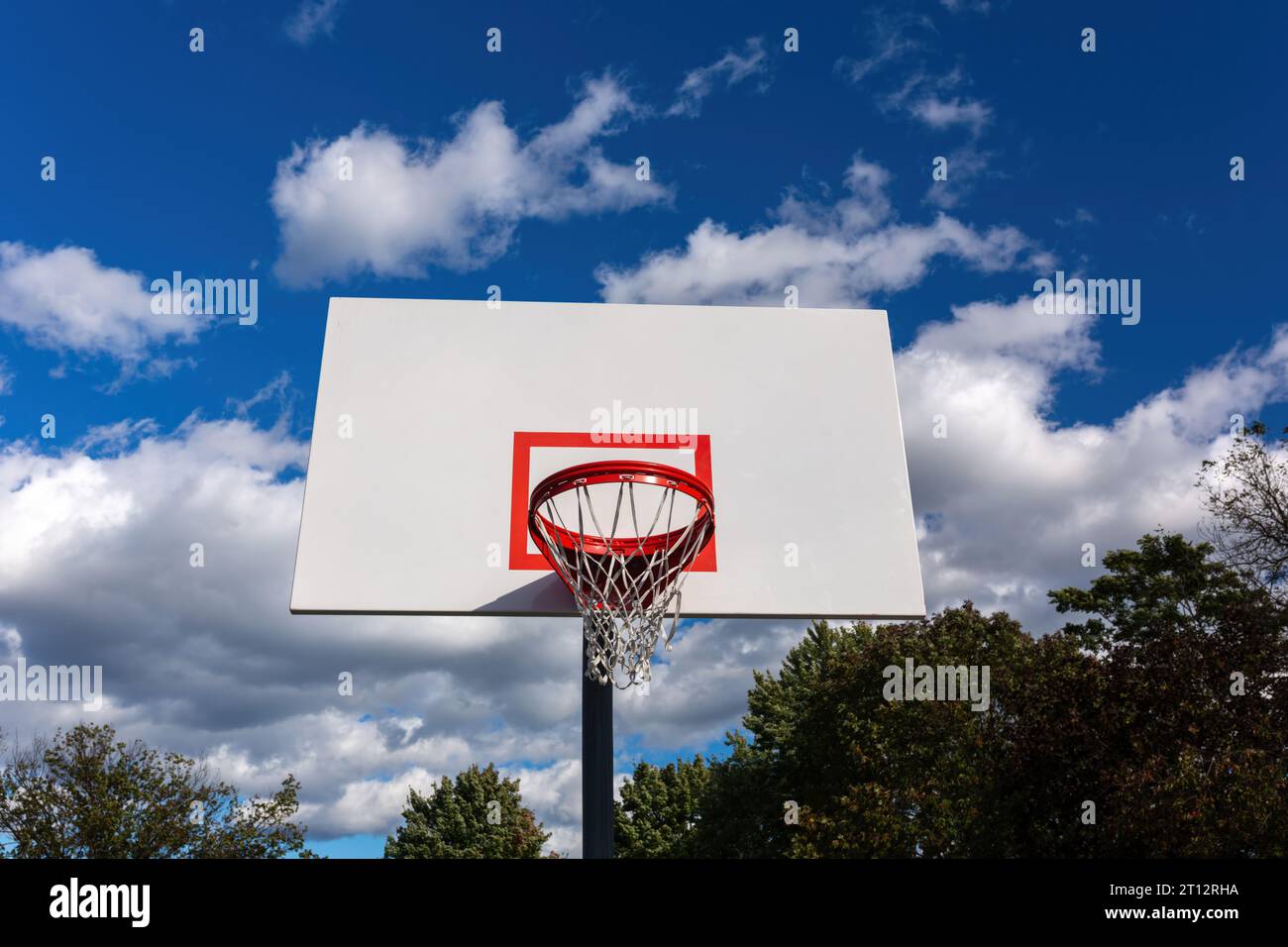 Un canestro da basket con una rete su un campo sullo sfondo di cieli azzurri e soffici nuvole bianche, che offre l'ambiente perfetto per gli sport all'aria aperta Foto Stock