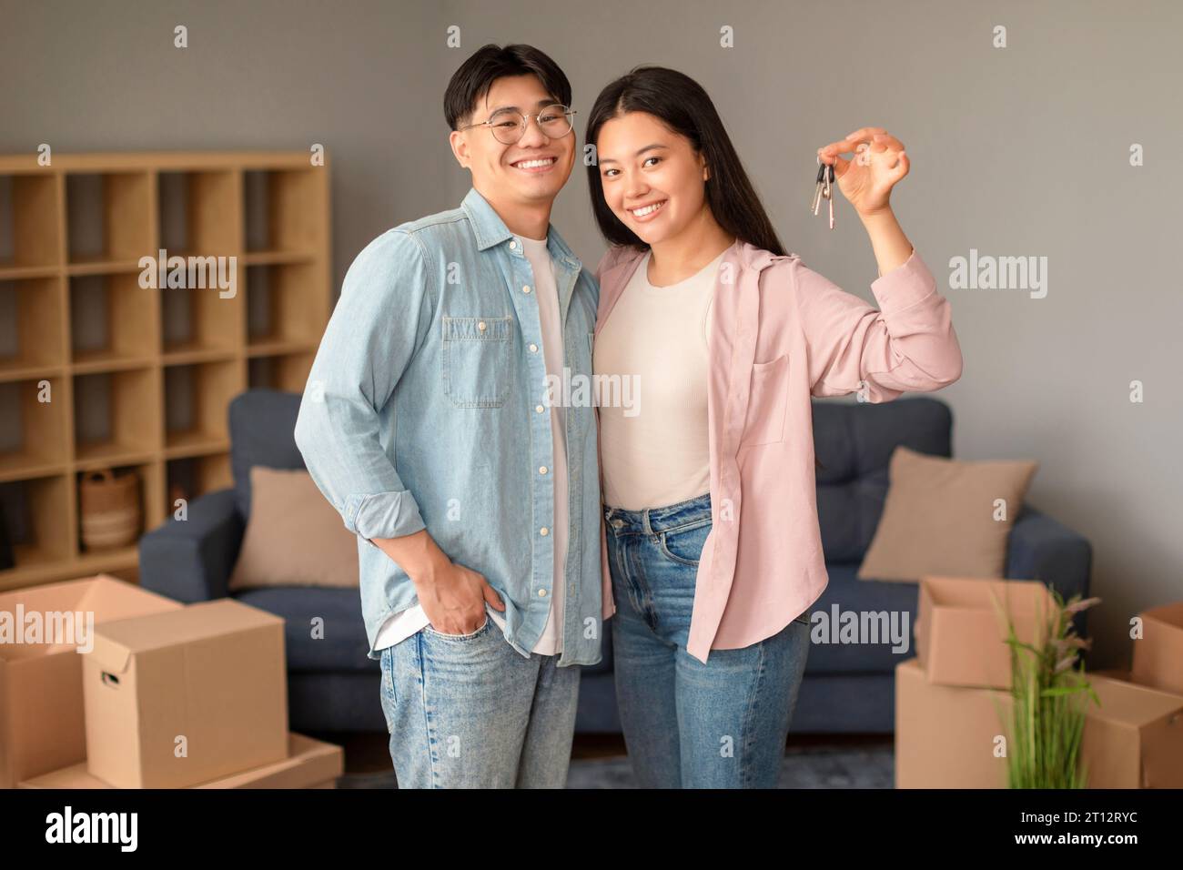 Gioiosa coppia cinese che tiene le chiavi di casa tra scatole mobili al coperto Foto Stock