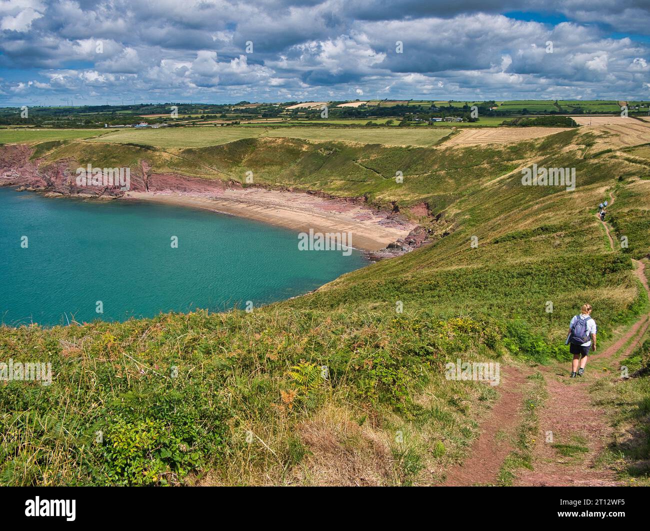 Gli amanti delle passeggiate lungo il sentiero costiero si avvicinano alla sabbia rossa della deserta Swanlake Beach nel Pembrokeshire, Galles, Regno Unito. In una giornata di sole d'estate con un turco Foto Stock