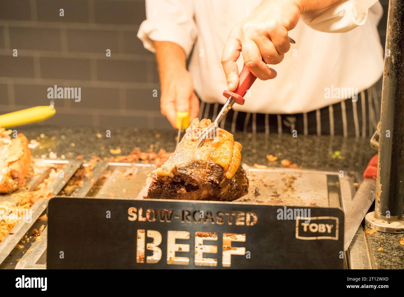 Lo chef affettò manzo arrosto lento posto sotto il banco di servizio riscaldato da servire al cliente al Toby Carvery Restaurant England Foto Stock