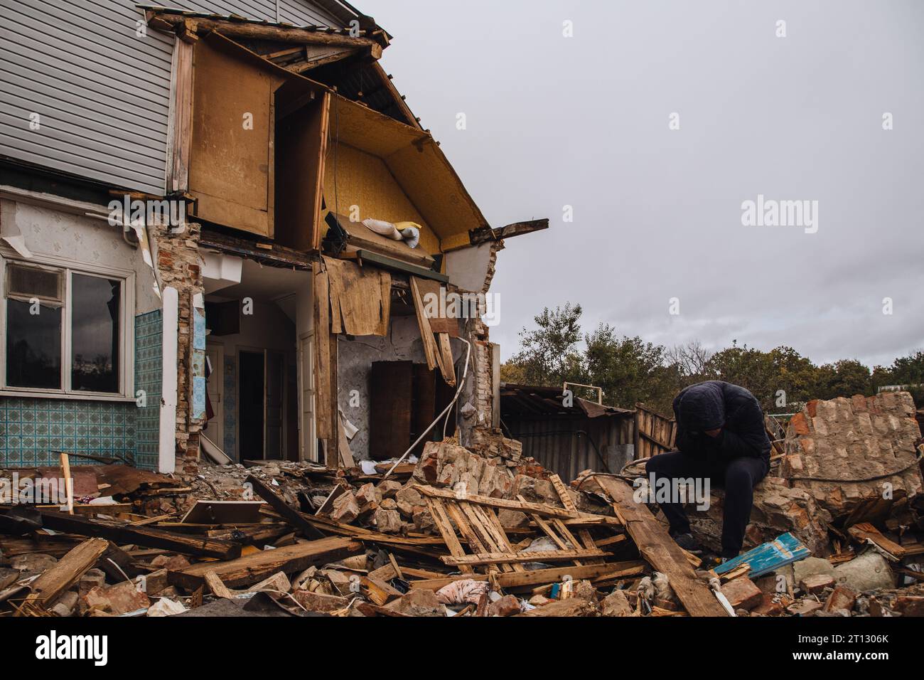 Un uomo triste in una casa in rovina. Senza speranza, senzatetto, risultato di conflitti militari e calamità naturali concetto. Foto Stock