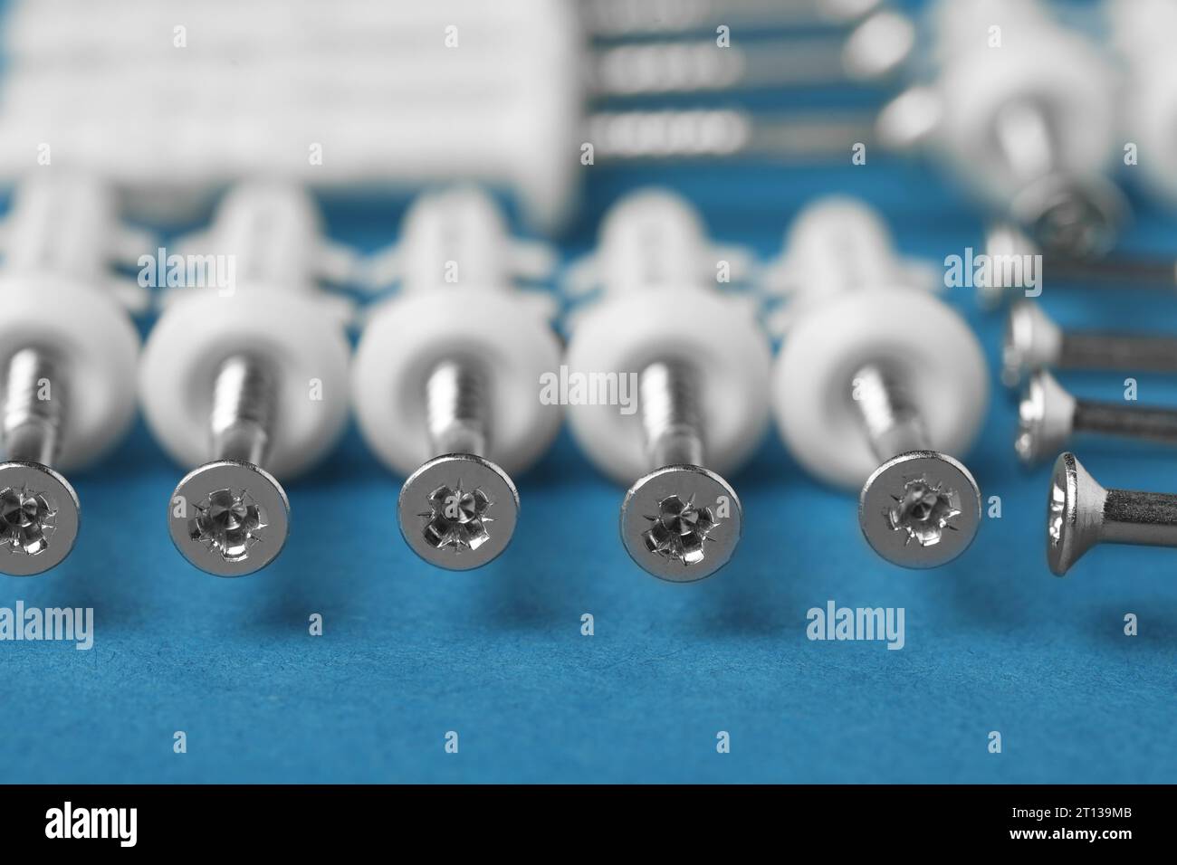 Molte viti metalliche con tasselli bianchi su sfondo blu, primo piano Foto Stock