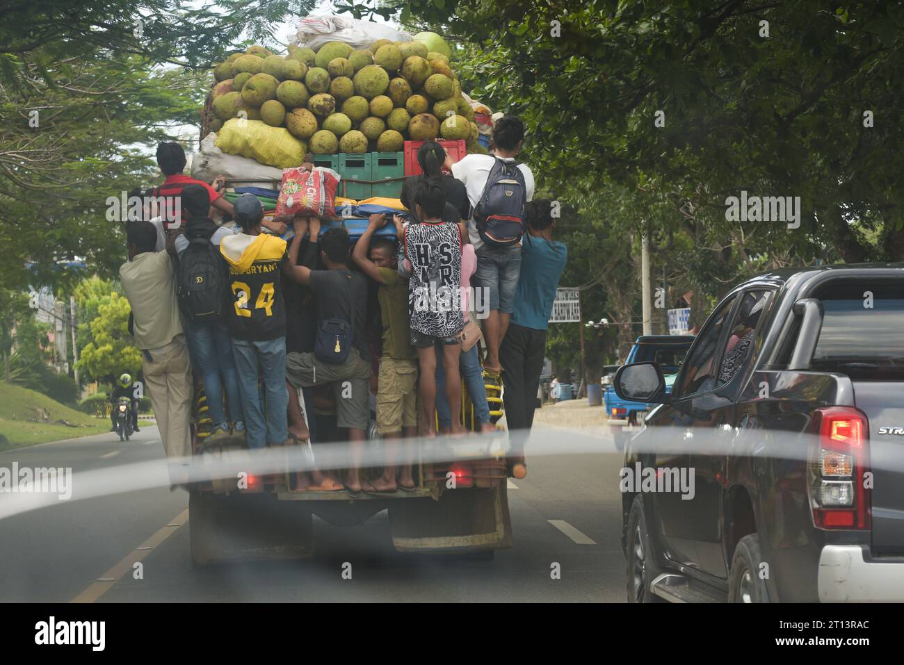 Cagayan de Oro, Filippine: I pendolari filippini si aggrappano al retro di una jeepney in movimento, piena di frutta e sacchi di verdura. Paese del terzo mondo. Foto Stock