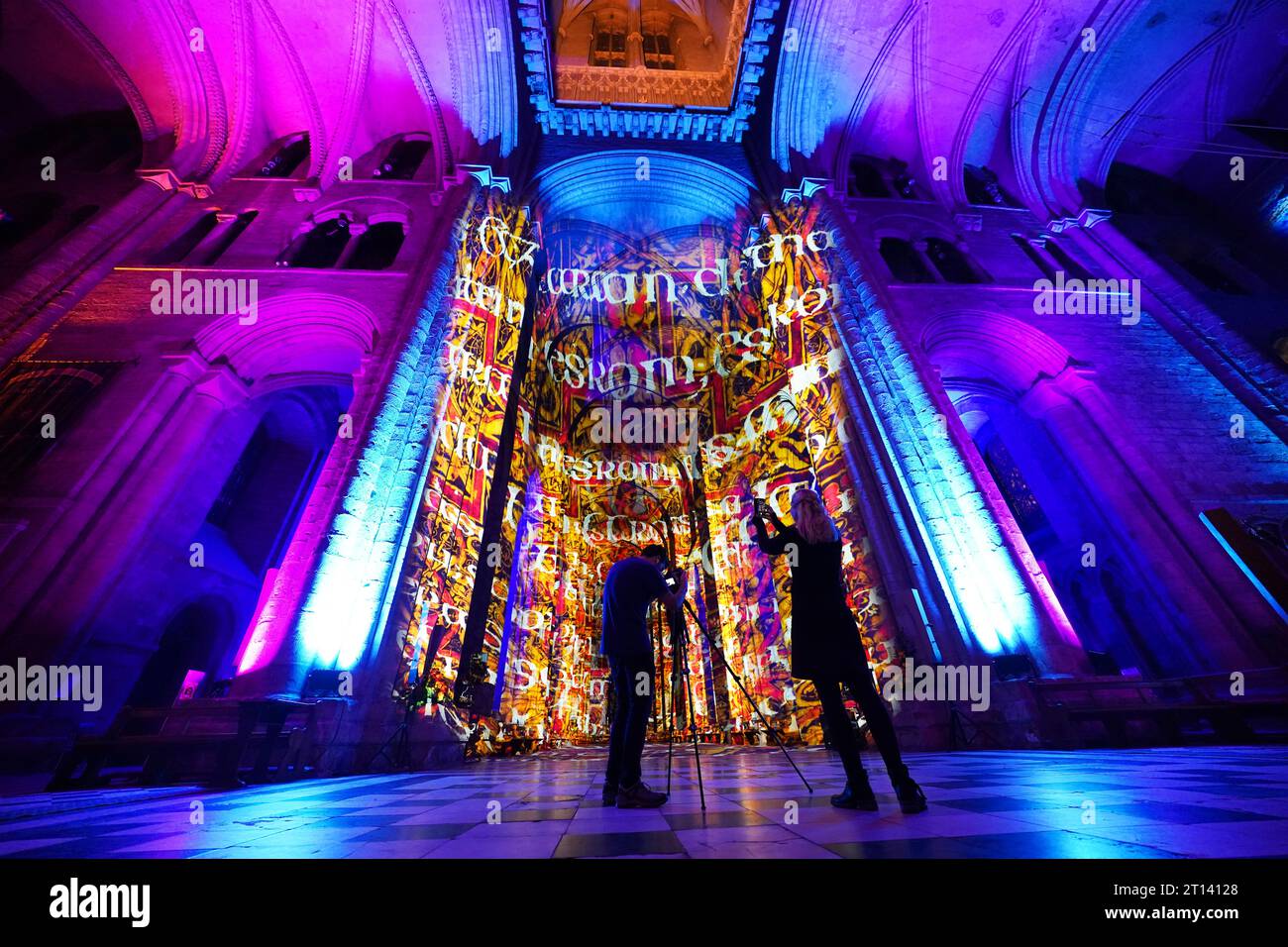 Persone che guardano le prove per lo spettacolo di luci Luxmurals dell'artista Peter Walker alla Cattedrale di Durham il martedì prima che apra al pubblico il mercoledì. Lo spettacolo di suoni e luci esplora la chimica e la biologia e interpreta artisticamente la scala delle cellule molecolari e del DNA, oltre ad esplorare la storia della scienza. Data immagine: Martedì 10 ottobre 2023. Foto Stock