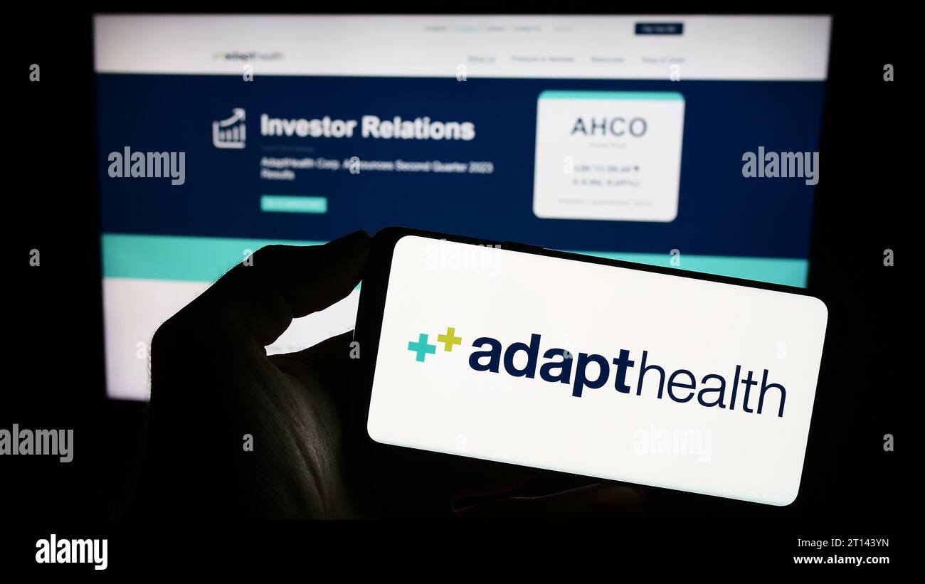Persona in possesso di smartphone con logo della società sanitaria statunitense AdaptHealth LLC di fronte al sito web. Concentrarsi sul display del telefono. Foto Stock
