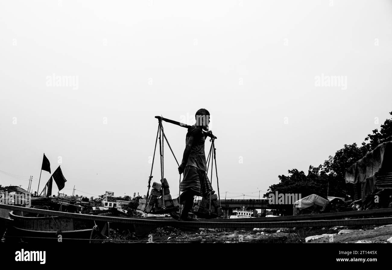 Persone che scaricano mattoni dalla barca, l'immagine scattata il 29 maggio 2022, da Amen Bazar, Bangladesh, dove i lavoratori sono impegnati a scaricare mattoni pesanti Foto Stock
