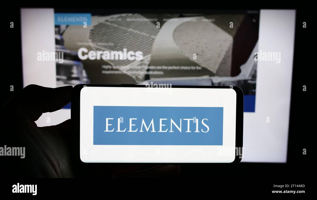 Persona in possesso di un cellulare con il logo della società britannica Elementis plc, azienda chimica specializzata, davanti alla pagina Web aziendale. Concentrarsi sul display del telefono. Foto Stock