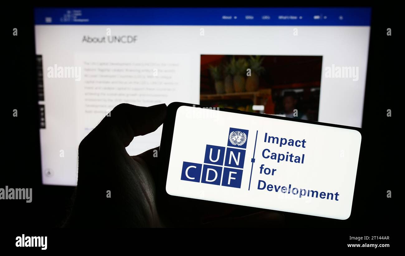 Persona che possiede un telefono cellulare con il logo del Fondo delle Nazioni Unite per lo sviluppo del capitale (UNCDF) davanti alla pagina web. Concentrarsi sul display del telefono. Foto Stock