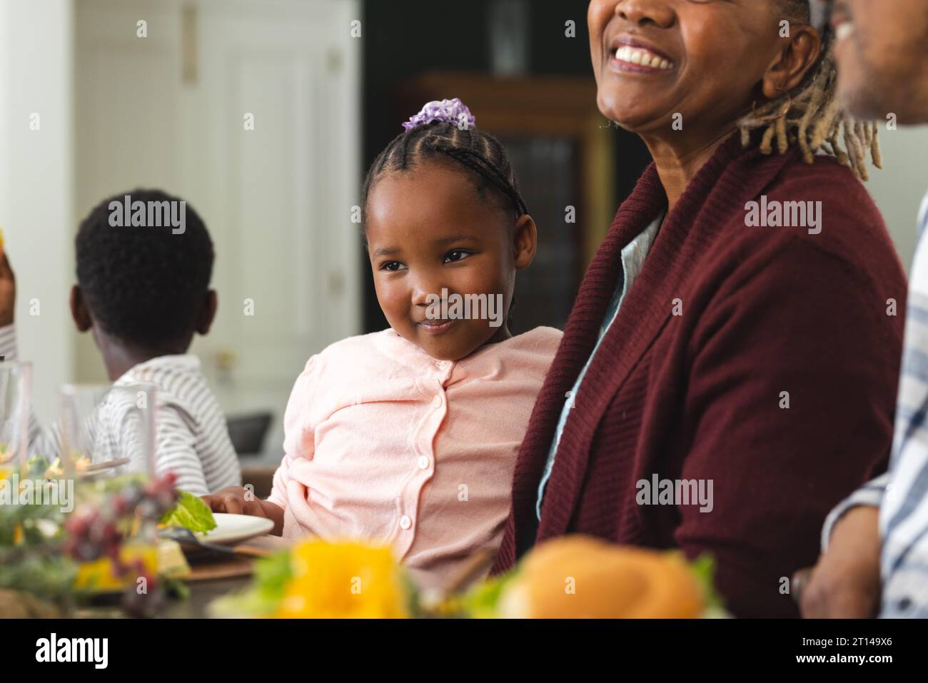 Nipote afroamericana seduta in braccio alla nonna durante la cena del Ringraziamento Foto Stock