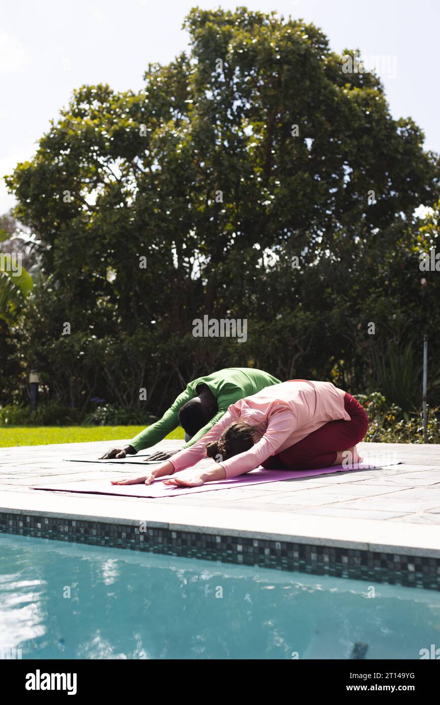 Coppie diverse che praticano yoga, distendendosi accanto alla piscina nel giardino soleggiato, spazio fotocopie Foto Stock