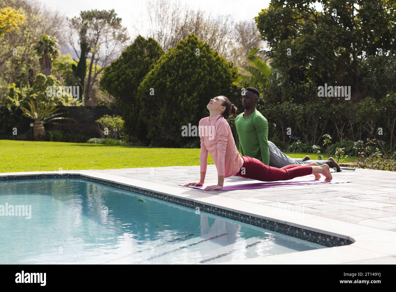 Coppia felice e variegata che pratica yoga, distendendosi accanto alla piscina nel giardino soleggiato, spazio fotocopie Foto Stock