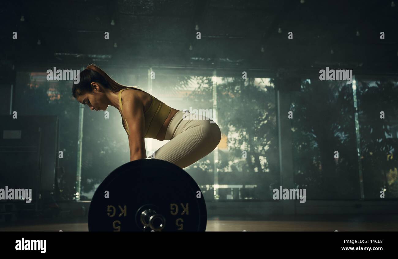 Giovane donna che fa deadlift con barra pesante in palestra, forte atleta femminile con pesi muscolari per il sollevamento del corpo, che si esercita con il campanello. Foto Stock
