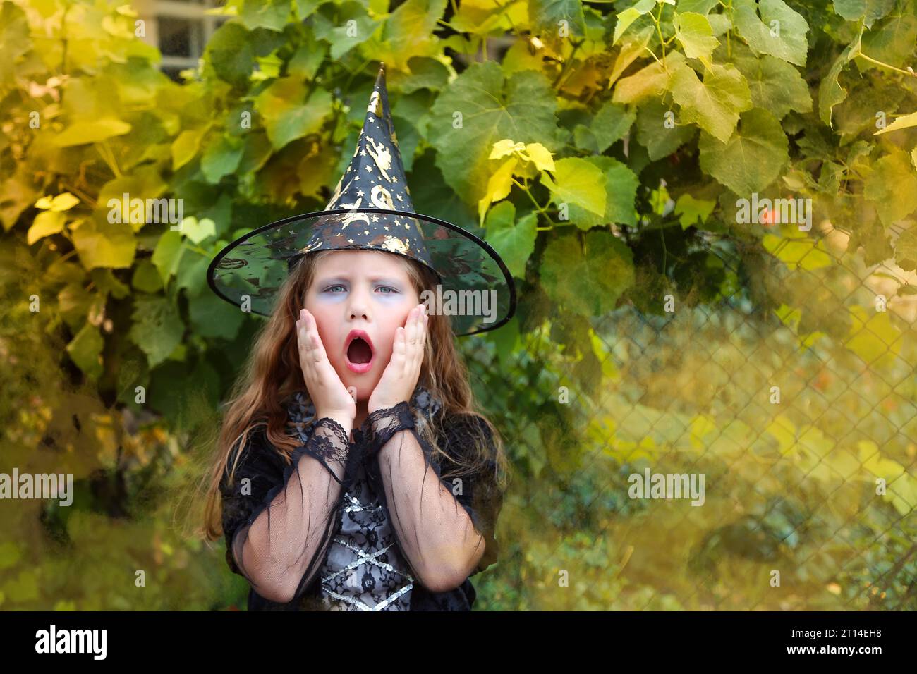 Halloween. piccola strega allegra con una bacchetta magica e il libro evocano e ridono. Foto Stock