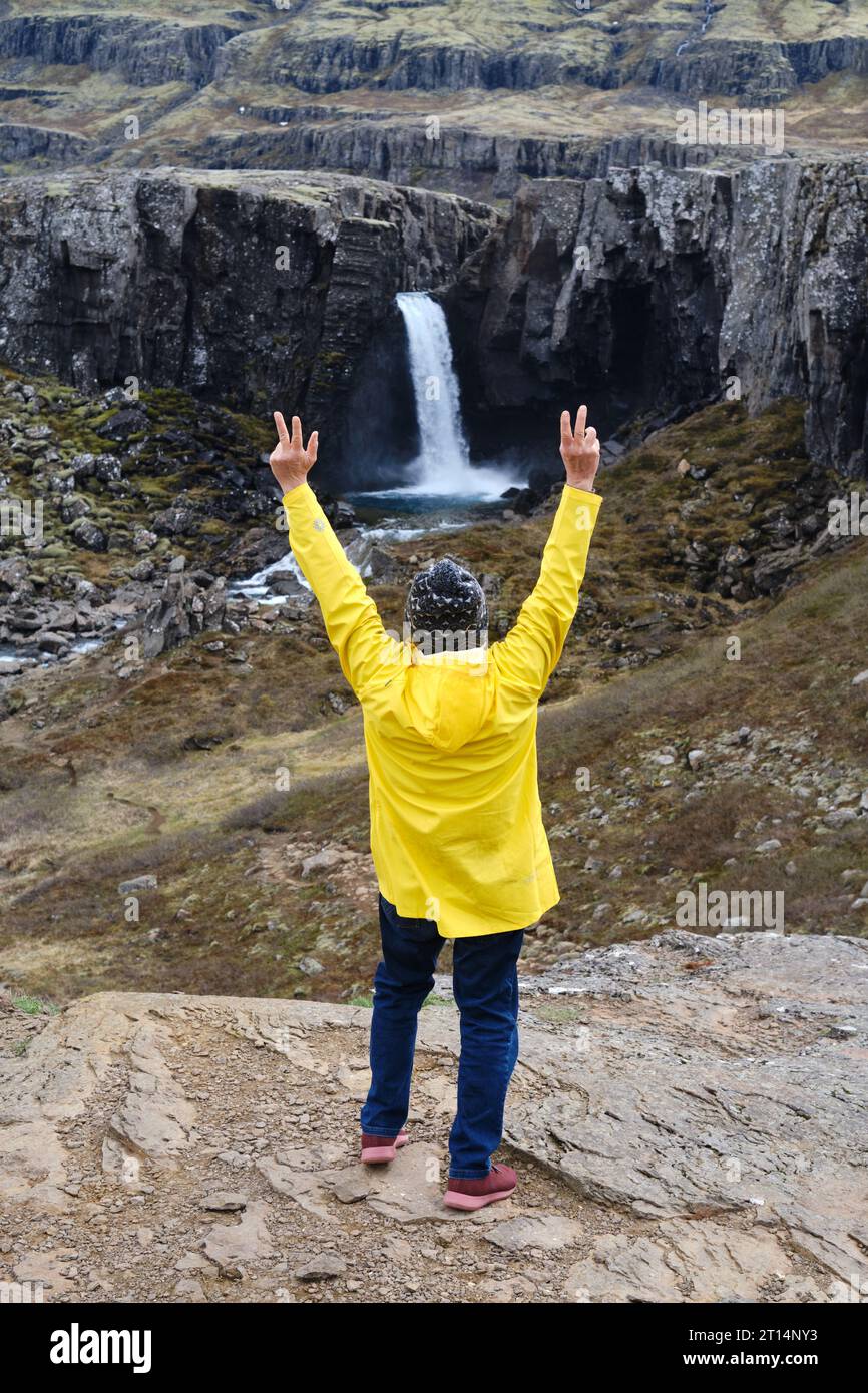 Un uomo su una giacca gialla di fronte a una splendida cascata islandese, che abbraccia la natura islandese Foto Stock