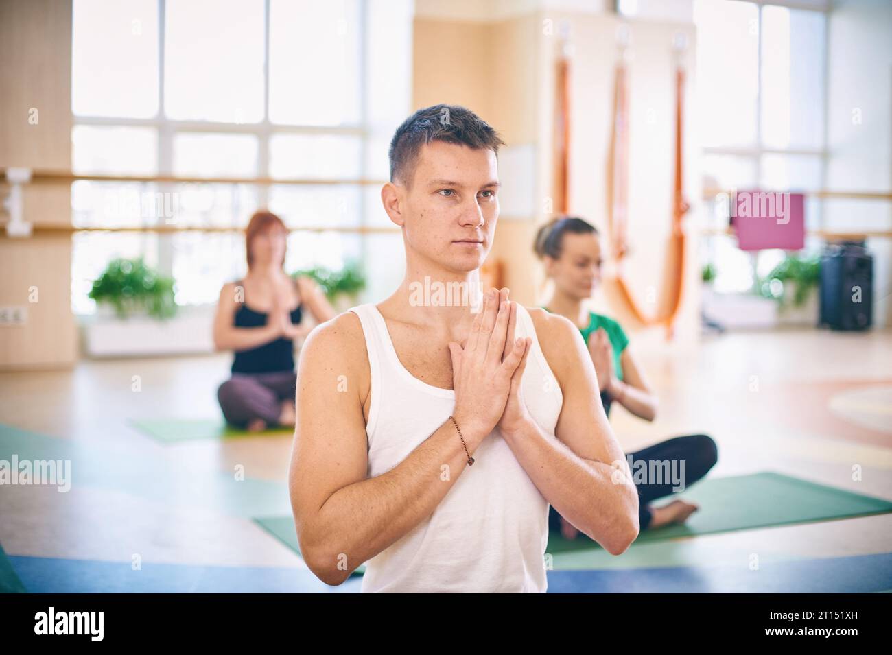 Gruppo di giovani sportivi che praticano lezioni di yoga con istruttore, seduti in allenamento Padmasana, posa del loto con mani piegate in namaste in yoga st Foto Stock