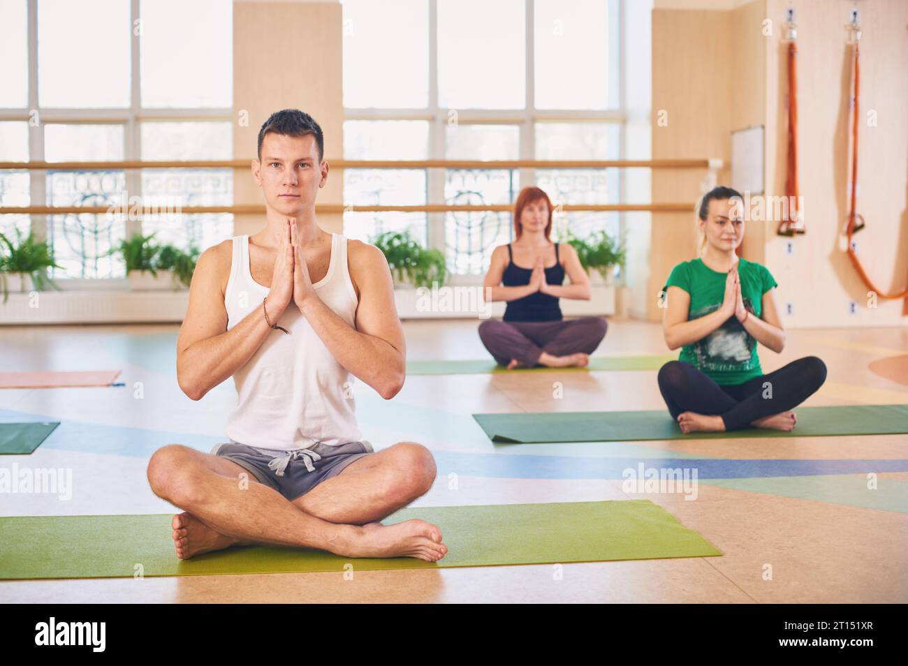 Gruppo di giovani sportivi che praticano lezioni di yoga con istruttore, seduti in allenamento Padmasana, posa del loto con mani piegate in namaste in yoga st Foto Stock