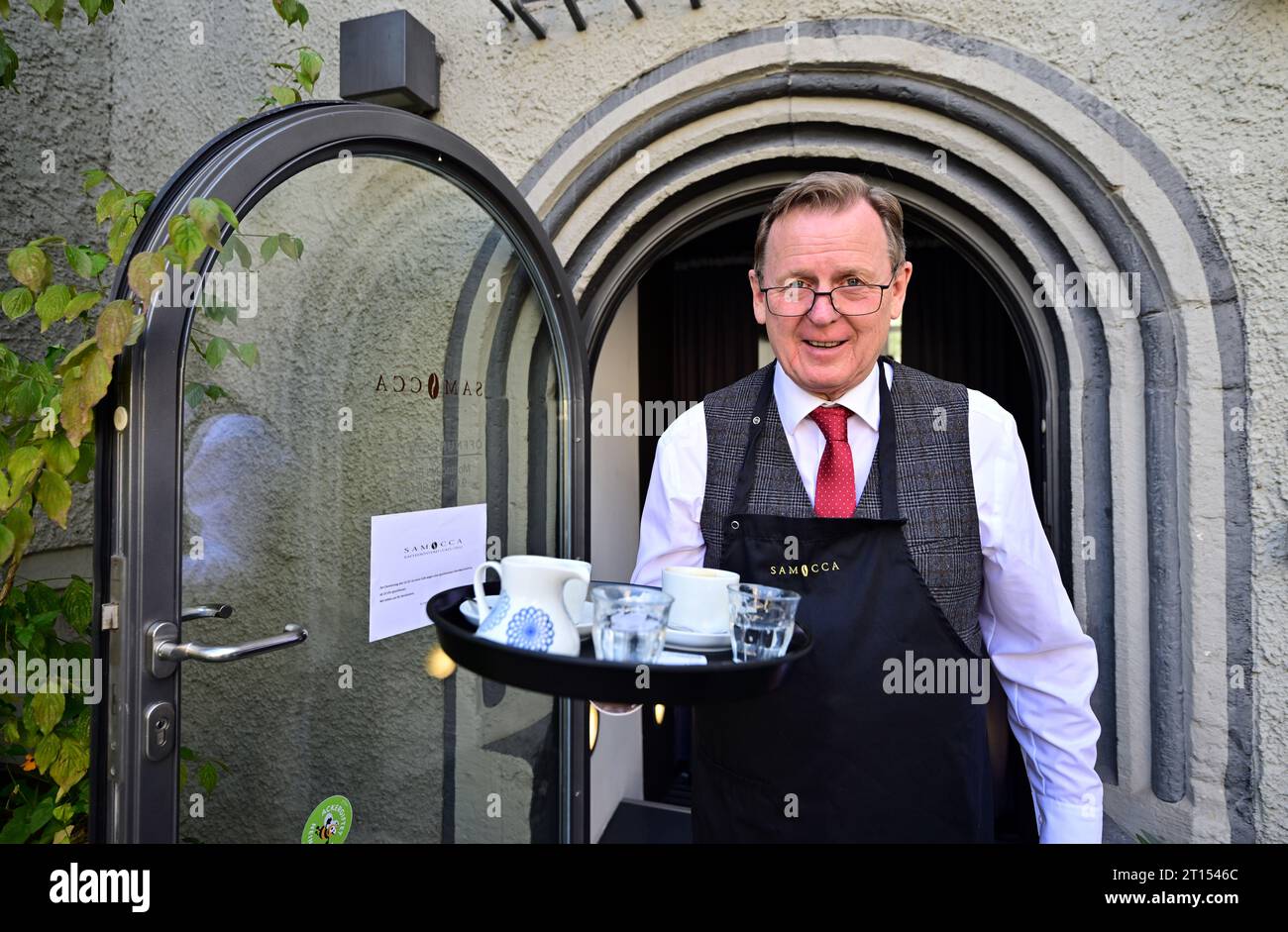 Weimar, Germania. 11 ottobre 2023. Bodo Ramelow (Die Linke), primo ministro della Turingia, serve specialità al caffè al Samocca Café Weimar. Nell'ambito del "cambio di turno", che si svolge ogni anno il 12 ottobre, le persone con e senza disabilità scambiano lavoro con un cambio di prospettiva. Quest'anno, per la prima volta, il Ministro Presidente della Turingia e la Cancelleria di Stato partecipano a questa giornata di azione. Il Samocca Café Weimar è un'operazione inclusiva del Diakoniestiftung Weimar Bad Lobenstein. Credito: Martin Schutt/dpa/Alamy Live News Foto Stock