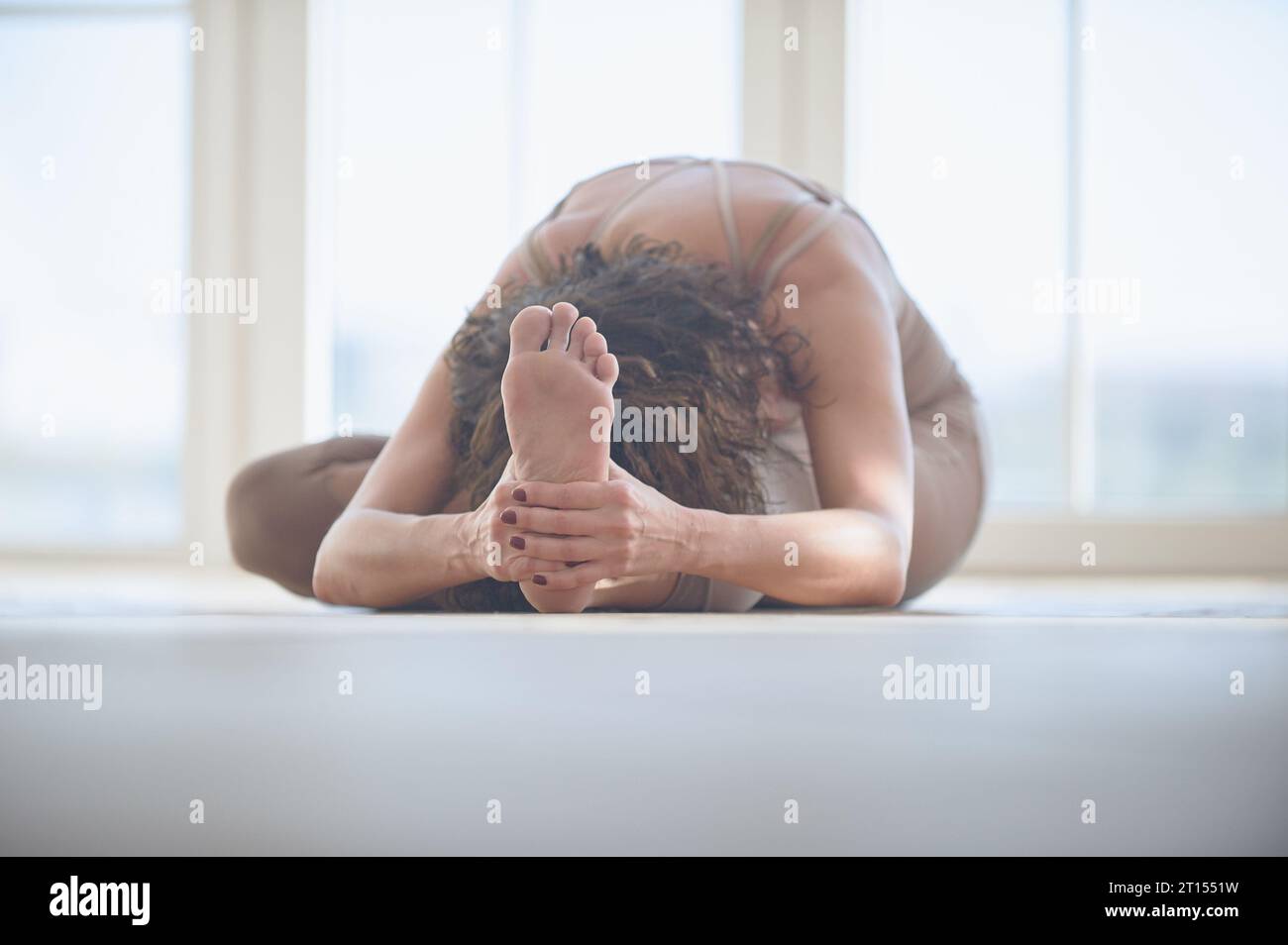 La bellissima giovane donna pratica yoga asana Janu Sirsasana nello studio di yoga leggero. Foto Stock