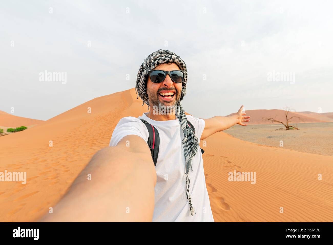 Happy man tramp in occhiali da sole scatta una foto selfie in il deserto sullo sfondo di una duna di bianco sabbia Foto Stock