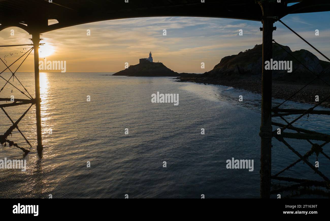 Alba al faro di Mumbles da sotto i supporti del Mumbles Pier sulla penisola di Gower a Swansea, Galles del Sud, Regno Unito Foto Stock