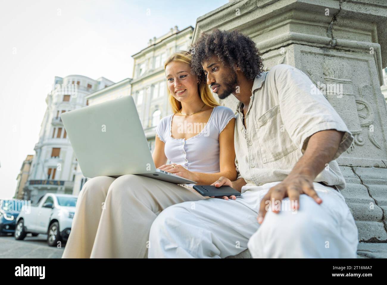 Due studenti usano il computer portatile insieme mentre studiano mentre sono seduti in città Foto Stock