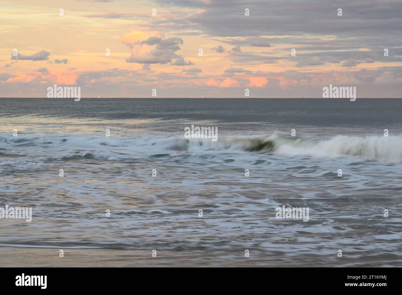 Onde che si infrangono sulla spiaggia di Ocean City, Maryland, mentre il sole tramonta illumina il cielo Foto Stock