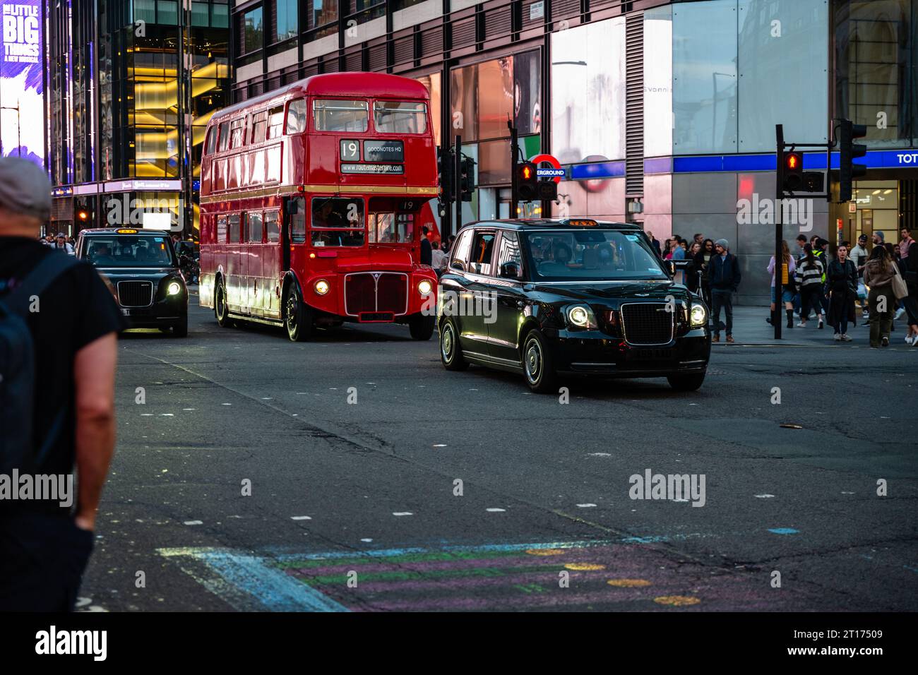 Londra, Inghilterra, 5 ottobre 2023: Un moderno taxi elettrico e un vecchio autobus a due piani passano davanti alla stazione della metropolitana di Tottenham Court Road. Foto Stock