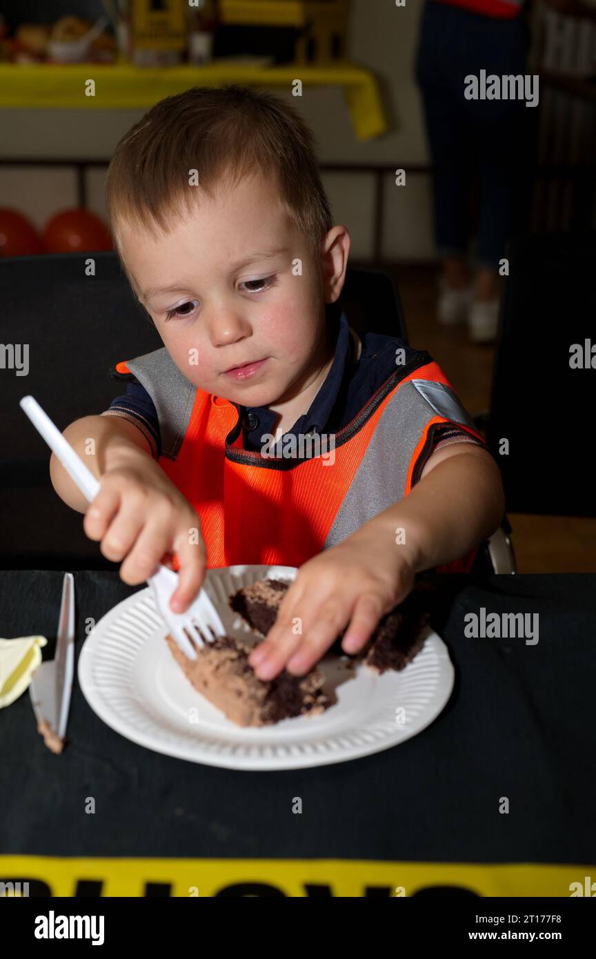 Il piccolo bambino seduto al tavolo a mangiare una torta Foto Stock