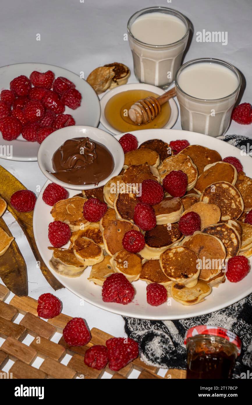 Mini pancake serviti con miele, cioccolato, burro di arachidi e latte. Servizio fotografico con menu gastronomico. Scatto selettivo della messa a fuoco. Foto Stock